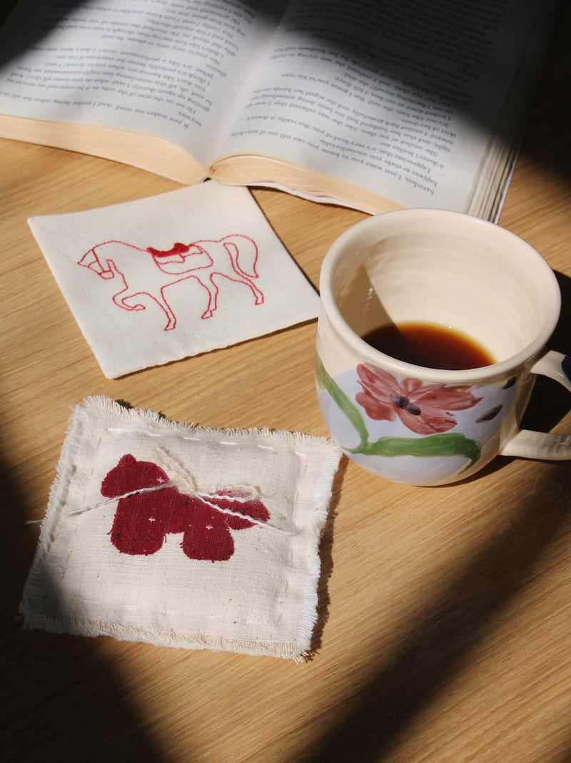 Handmade fabric coaster with embroidered horse motif, artisan textile coaster on wooden table with ceramic mug, aesthetic home decor for cozy coffee moments