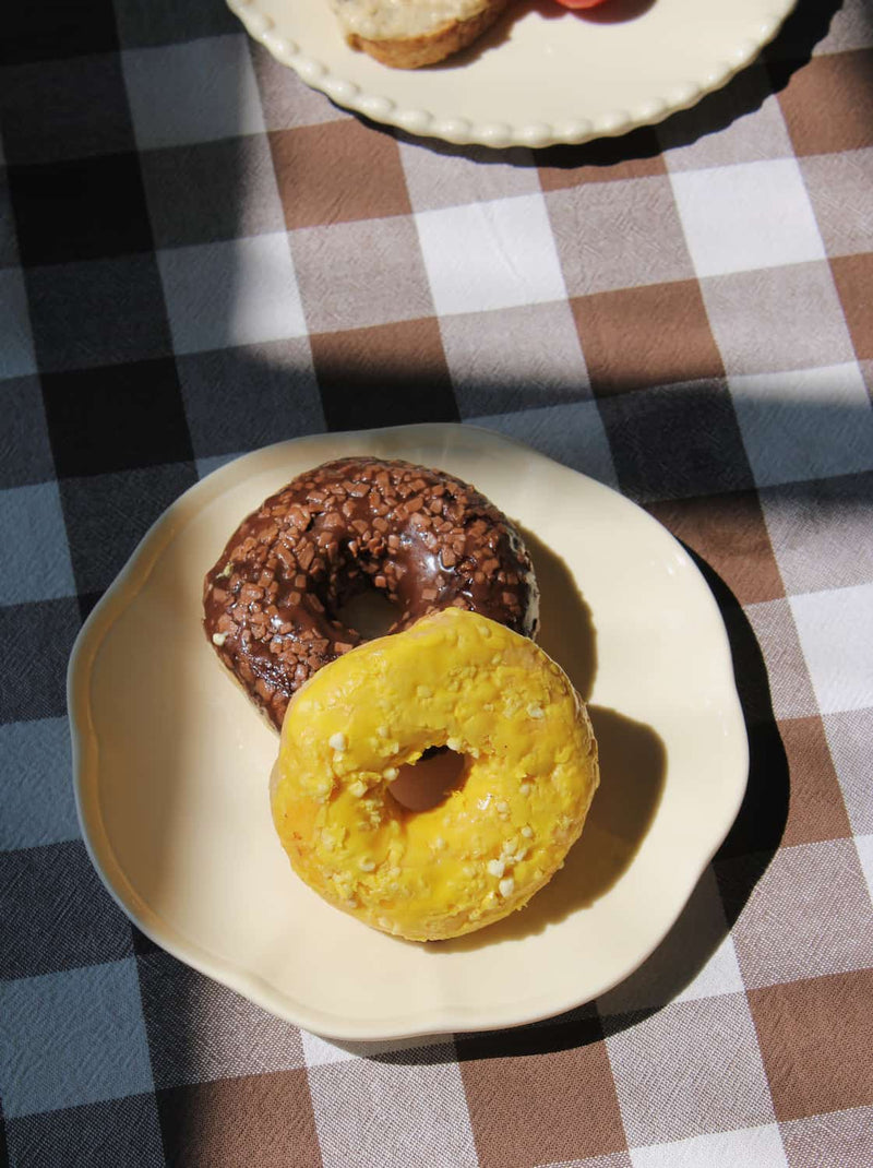 Two donuts on a plate with a checkered tablecloth in the background