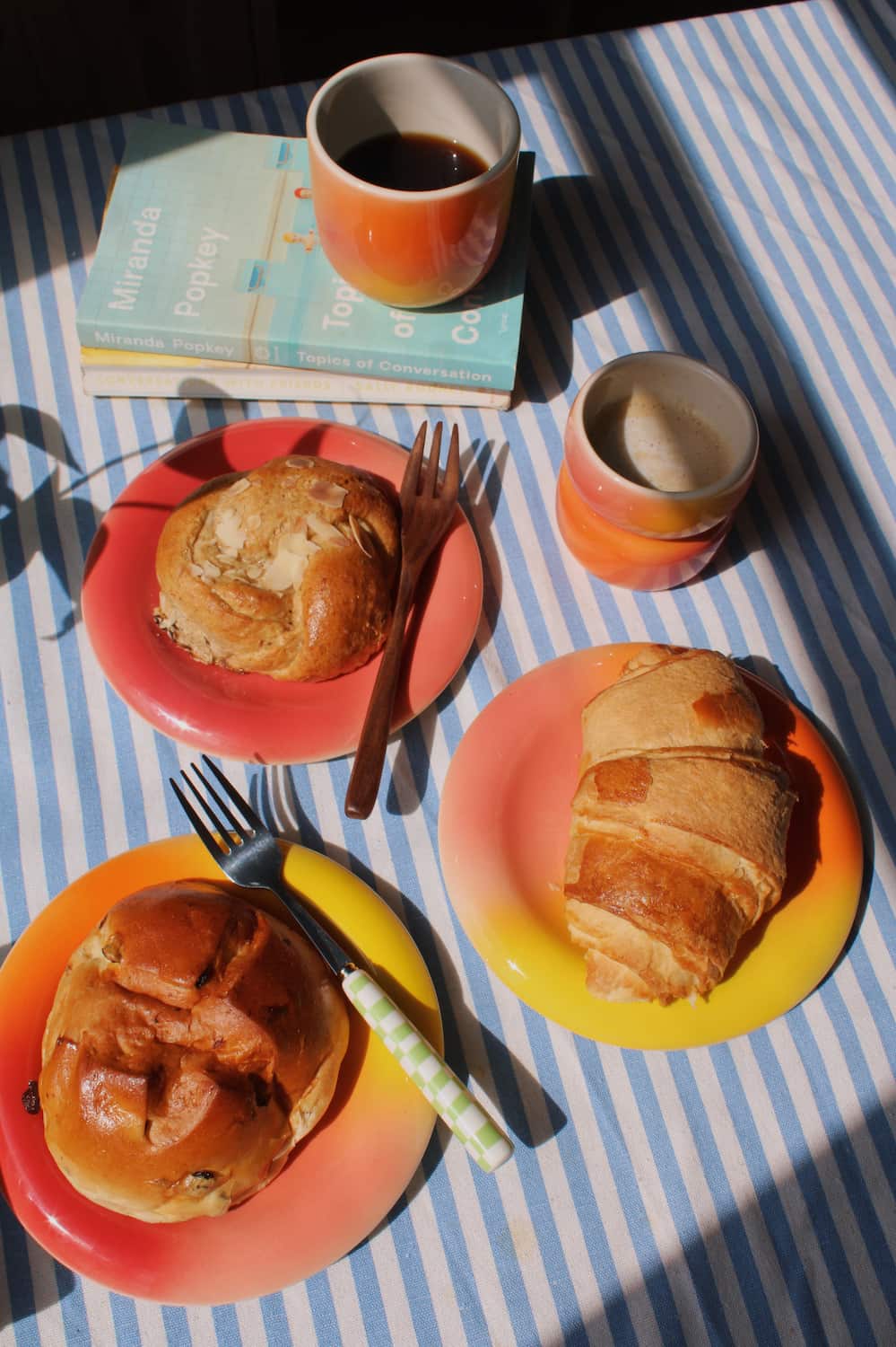 Handmade ceramic cups and colourful gradient plates by Agata Puławska, styled with coffee and pastries on a blue striped tablecloth