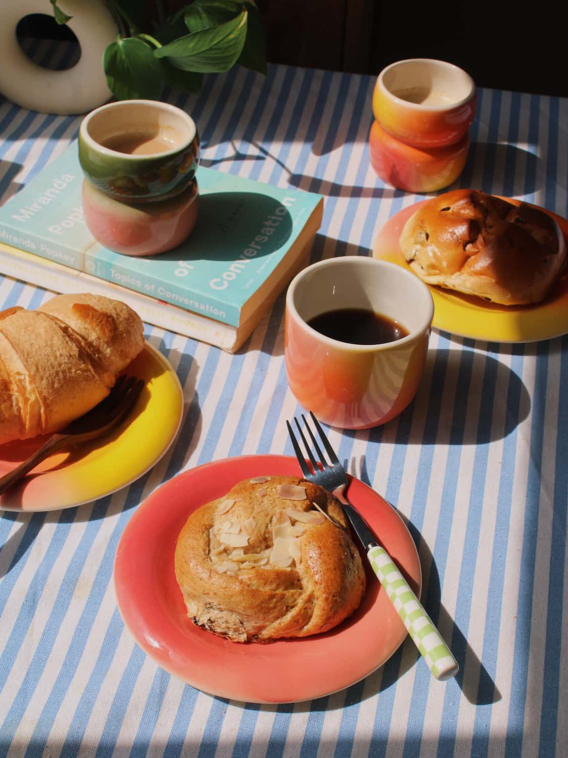 Handmade ceramics by Agata Puławska – colourful ceramic cups and plates styled with coffee and pastries on a blue striped tablecloth