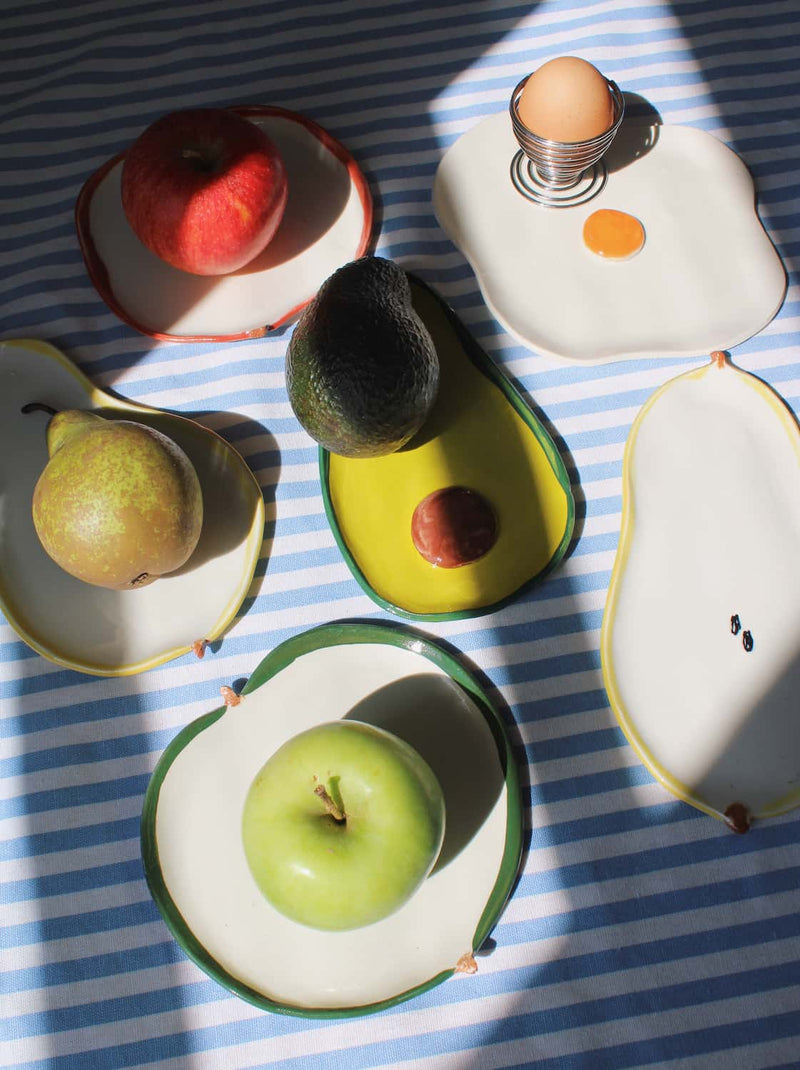 Ceramic spoon rests in fruit shapes including pear, apple, avocado, and fried egg designs