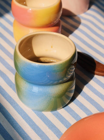 Handmade Belly Dew ceramic cup in soft green glaze on striped tablecloth with natural light