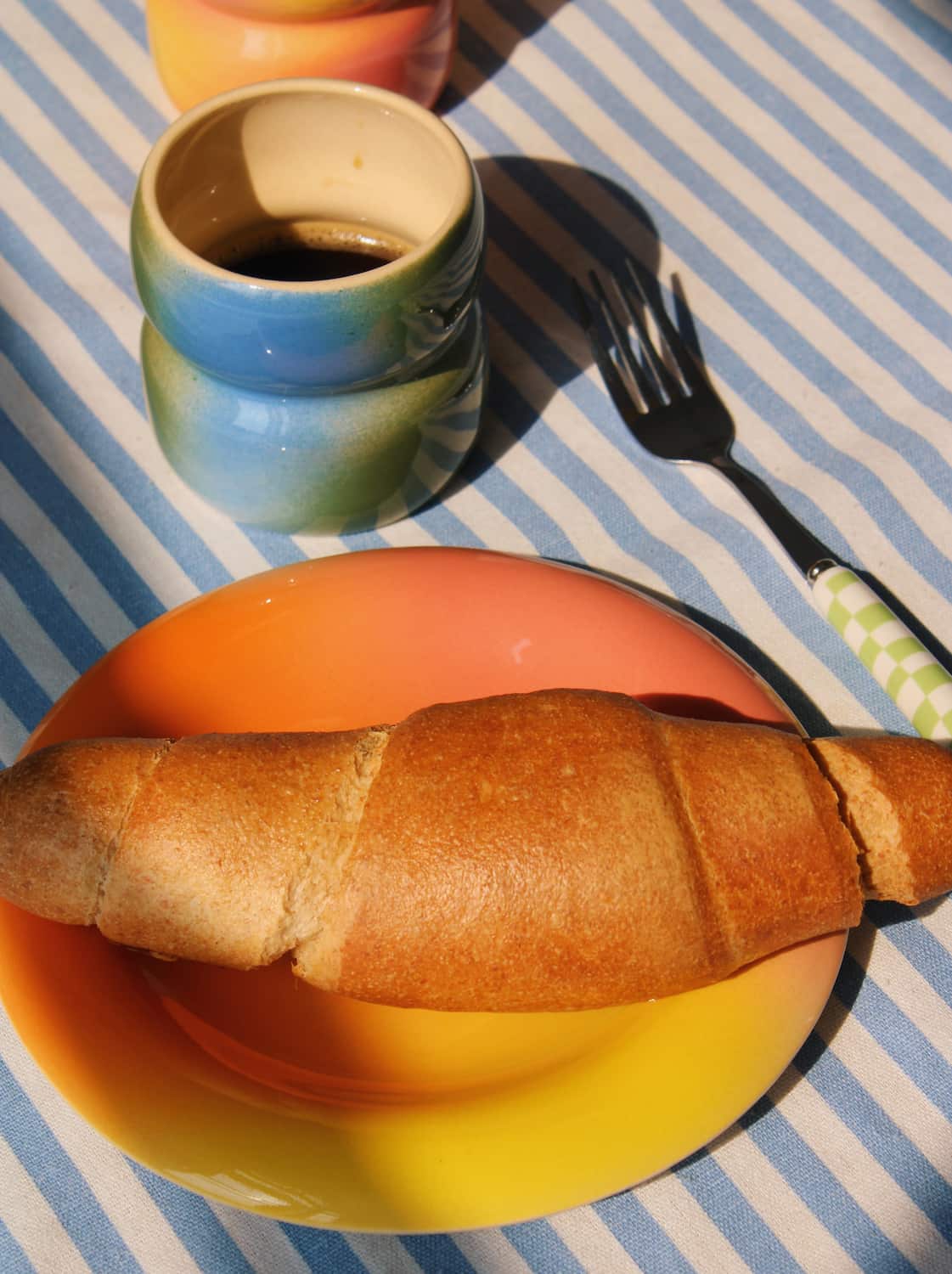 Belly Dew ceramic cup styled with croissant and breakfast plate on striped tablecloth