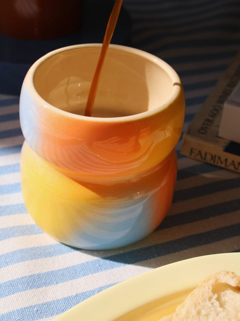 Gradient-colored mug being filled with a liquid on a striped surface