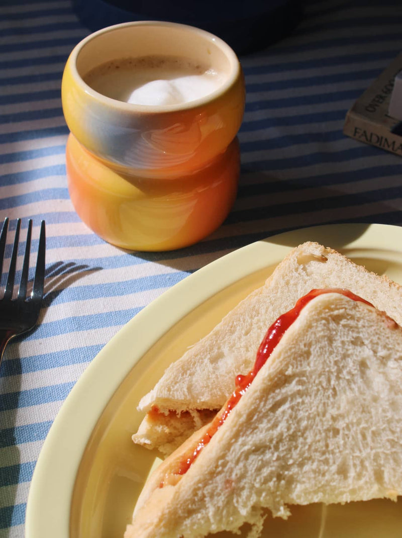 Triangular sandwich with jelly on a plate with a blurred cup of coffee in the background.
