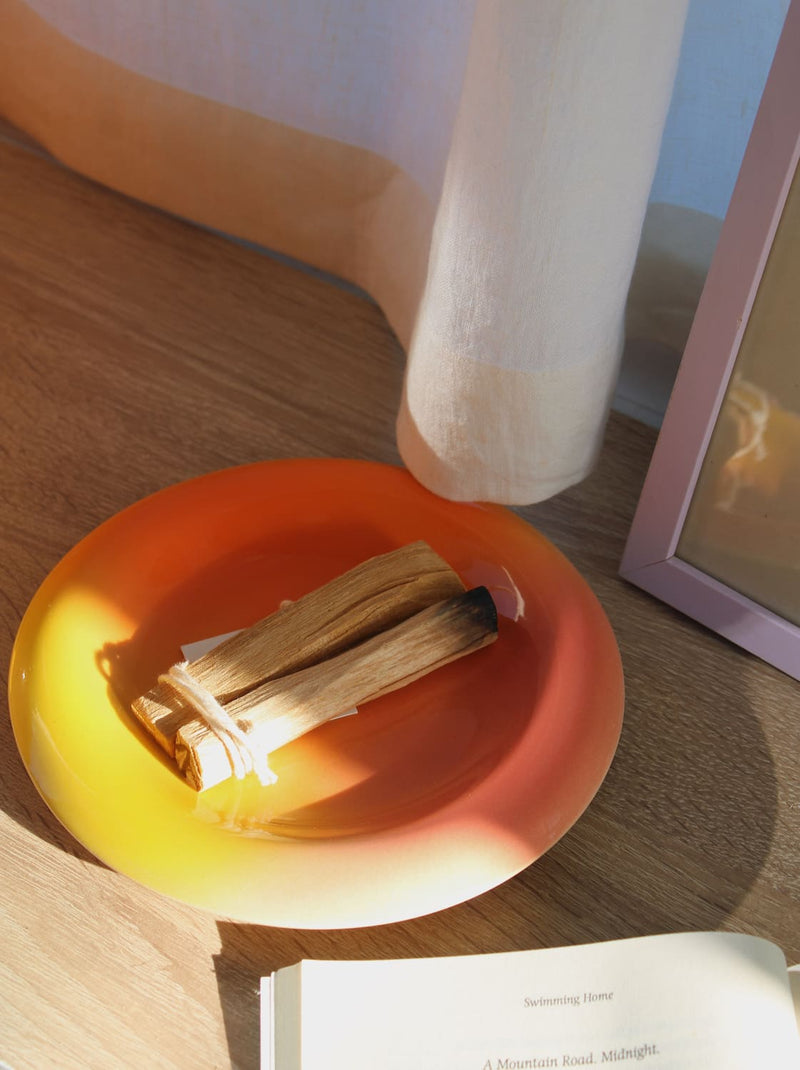 Belly Sunset plate in gradient yellow to red-orange glaze, styled with palo santo sticks on an oak surface