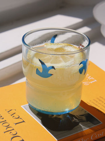 Glass of lemonade with blue bird illustrations on a magazine