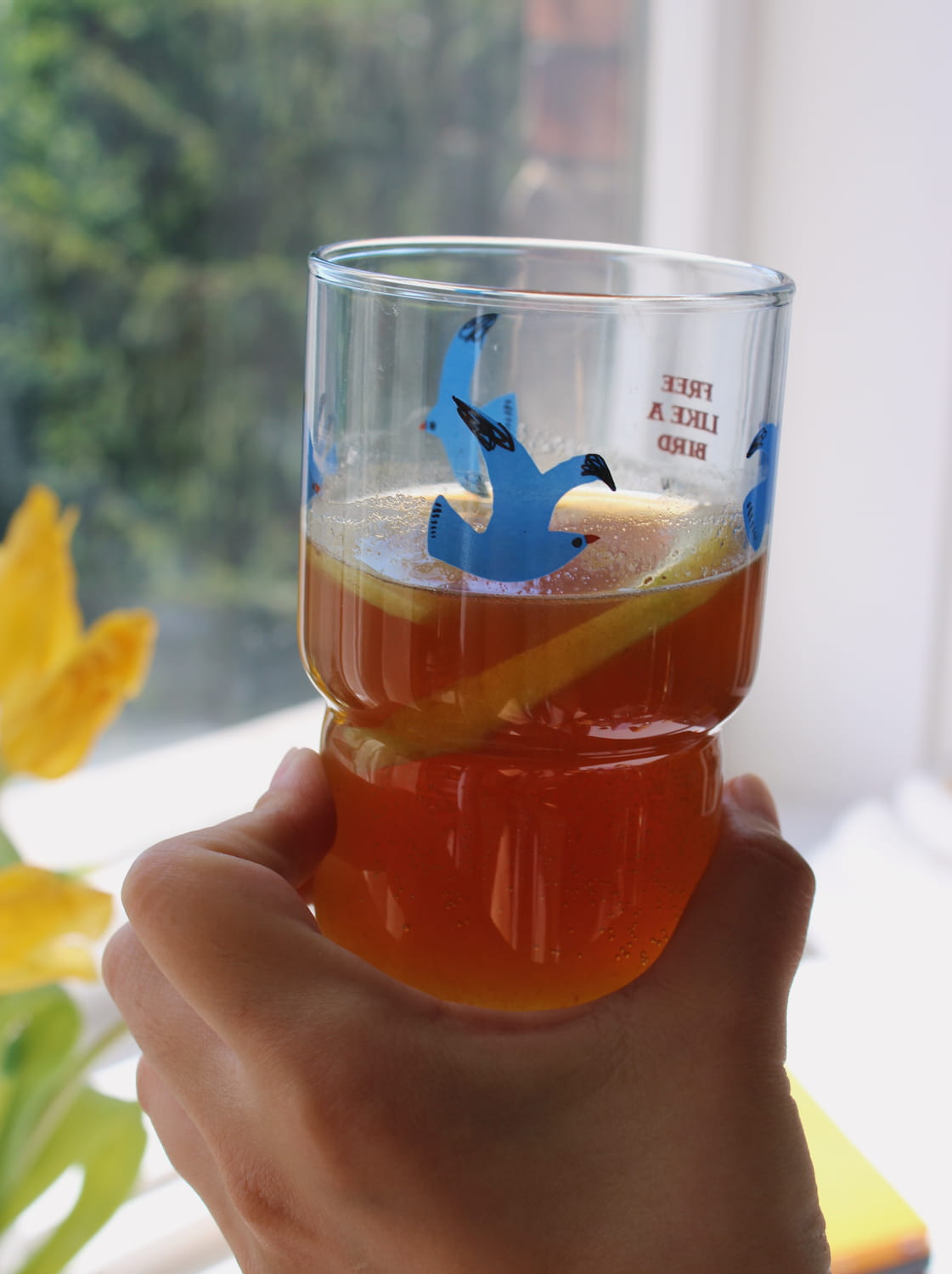 Hand holding a glass of iced tea with lemon slices and blue bird design.