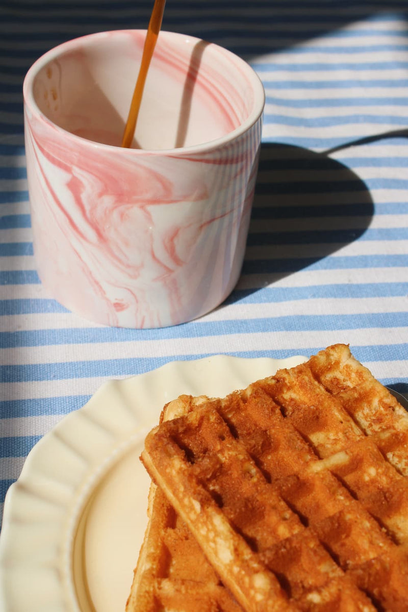 Blush pink ceramic cup with coffee and waffle in warm morning sunlight