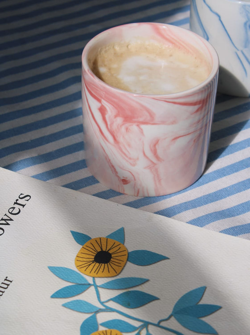 Blush ceramic cup with soft pink glaze styled on striped tablecloth in natural light