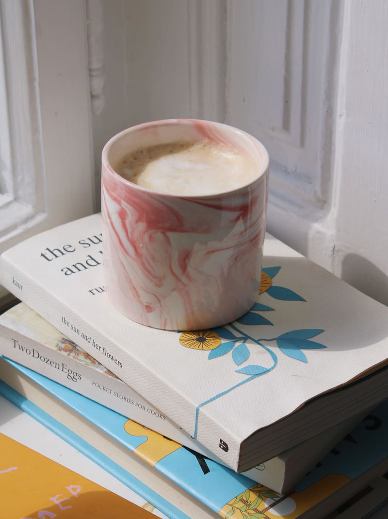 Handmade blush ceramic cup with marbled pink tones on books and breakfast table