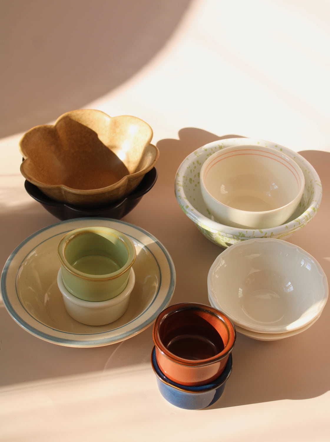 Assorted handmade ceramic bowls and cups in soft pastel glazes, styled in warm natural light