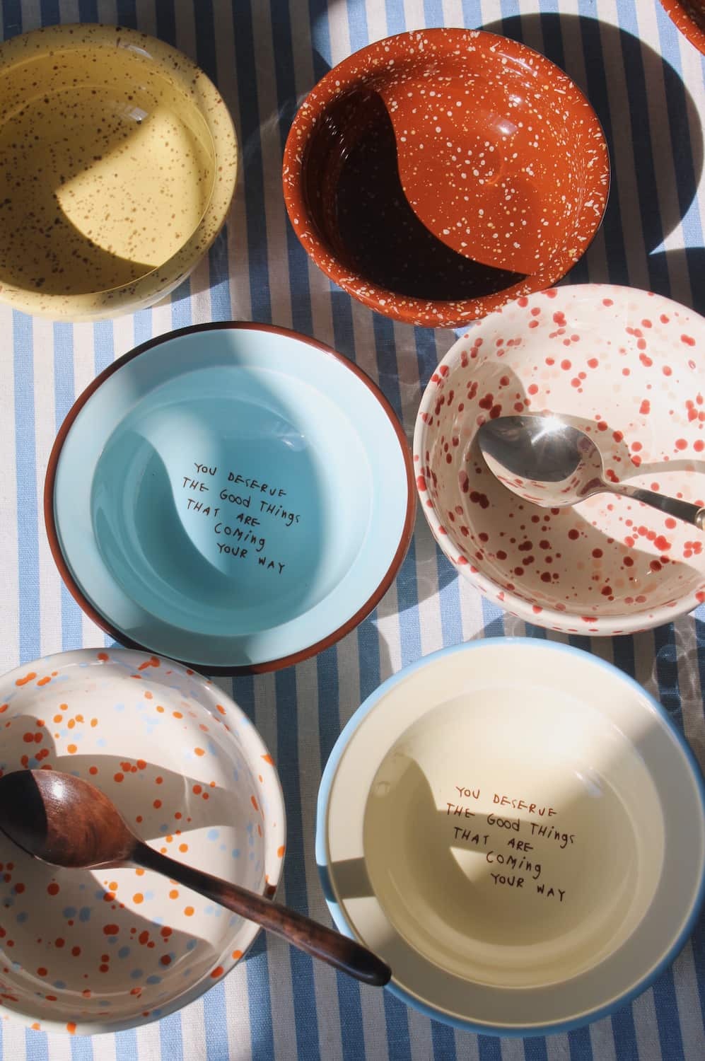 Collection of ceramic bowls with speckled patterns and text on a striped tablecloth.