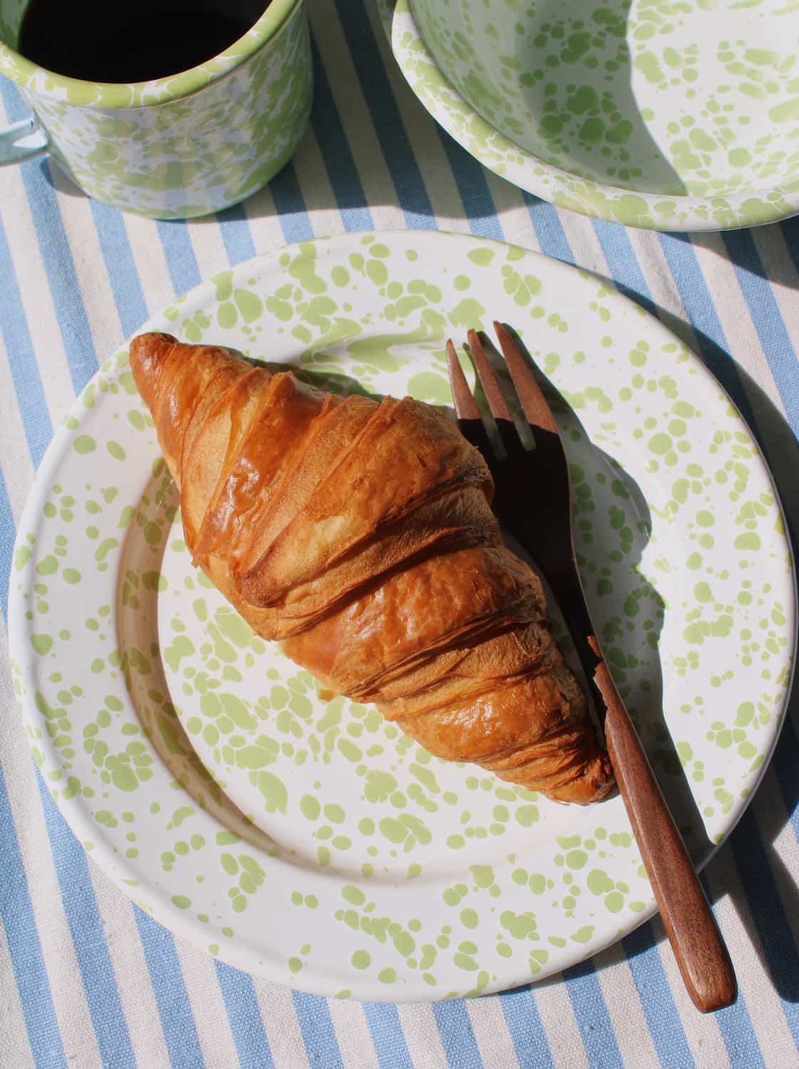 Clover enamel plate with croissant and matching enamel tableware in cozy setting
