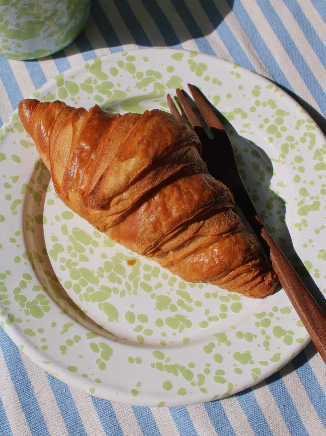 Croissant on a patterned plate with a knife on a striped tablecloth