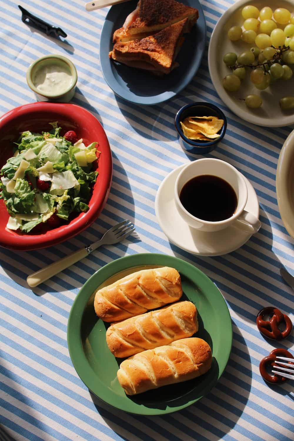 Modern Table setting with pastries, coffee, salad, and fruit on a striped tablecloth.