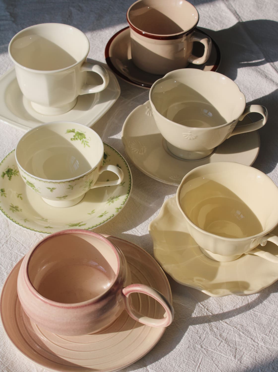 Handmade ceramic cup and saucer sets arranged on a table, featuring soft neutral tones and vintage-inspired designs for coffee and tea.