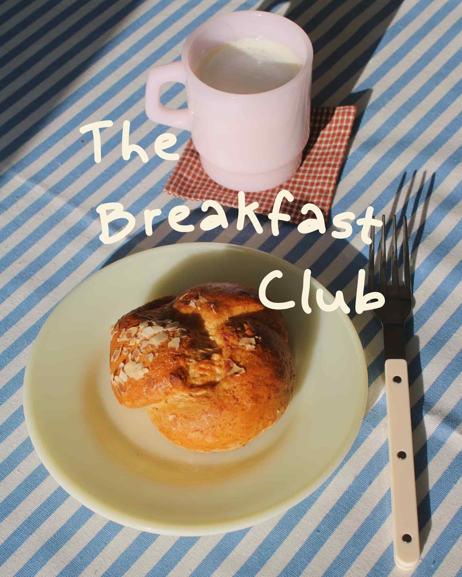 White ceramic mug and handmade plate styled with sourdough bread and cutlery on a blue striped tablecloth, with hand-lettered text reading The Breakfast Club