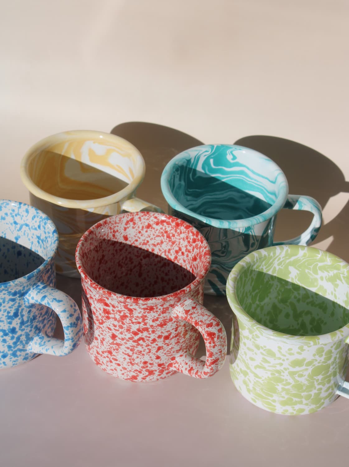 Handmade ceramic mugs in colorful marbled glazes arranged in soft natural sunlight