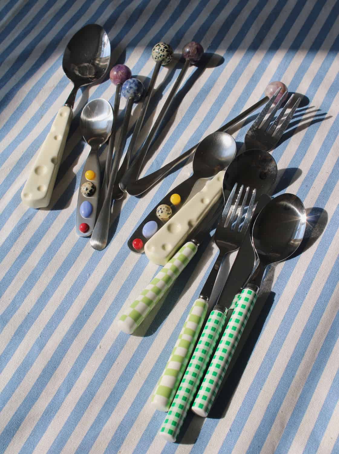 A set of decorative cutlery including spoons, forks, and knives with colorful, patterned handles, arranged on a blue and white striped fabric background.