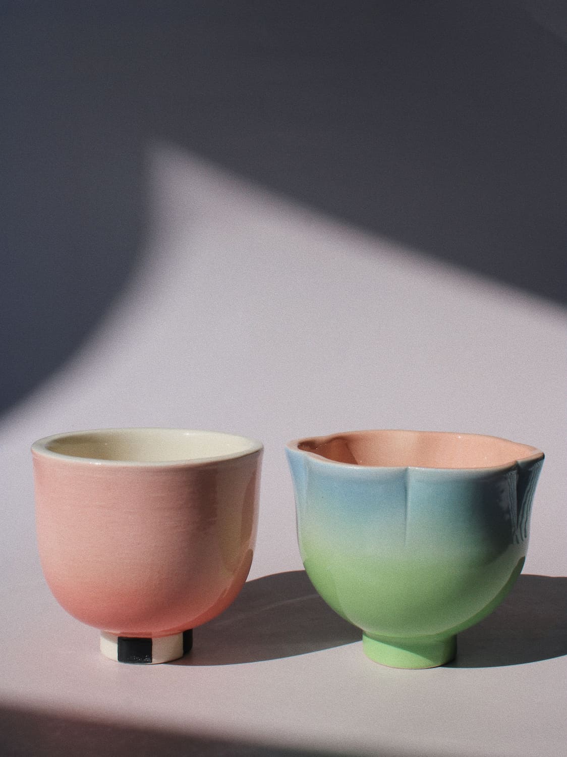 Two handmade ceramic cups from the Yunomi collection side by side against a pink background