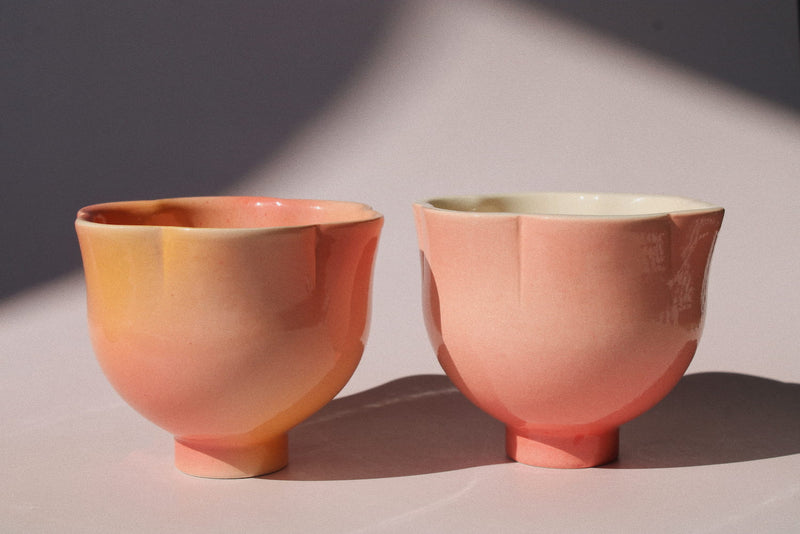 Two handmade ceramic cups from the Yunomi collection side by side against a pink background