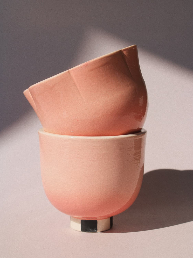Two stacked ceramic bowls in a matte dusty pink color, set against a neutral background with soft shadows.