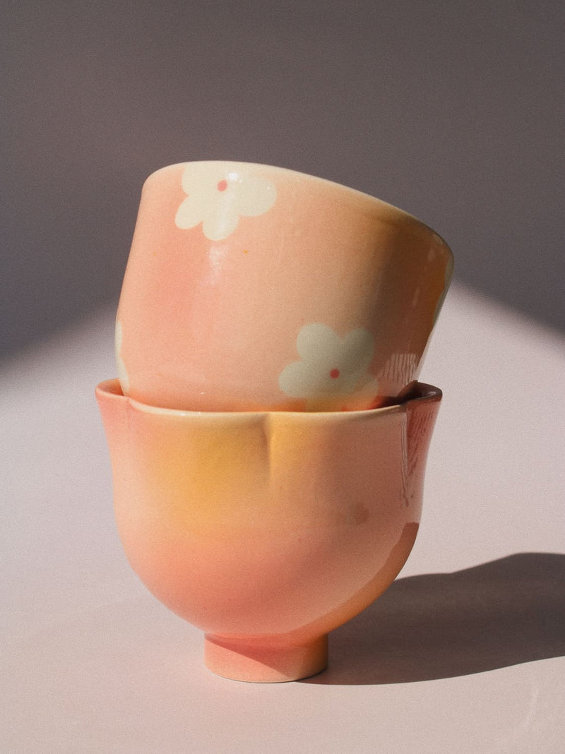 Two handmade ceramic cups from the Yunomi collection side by side against a pink background