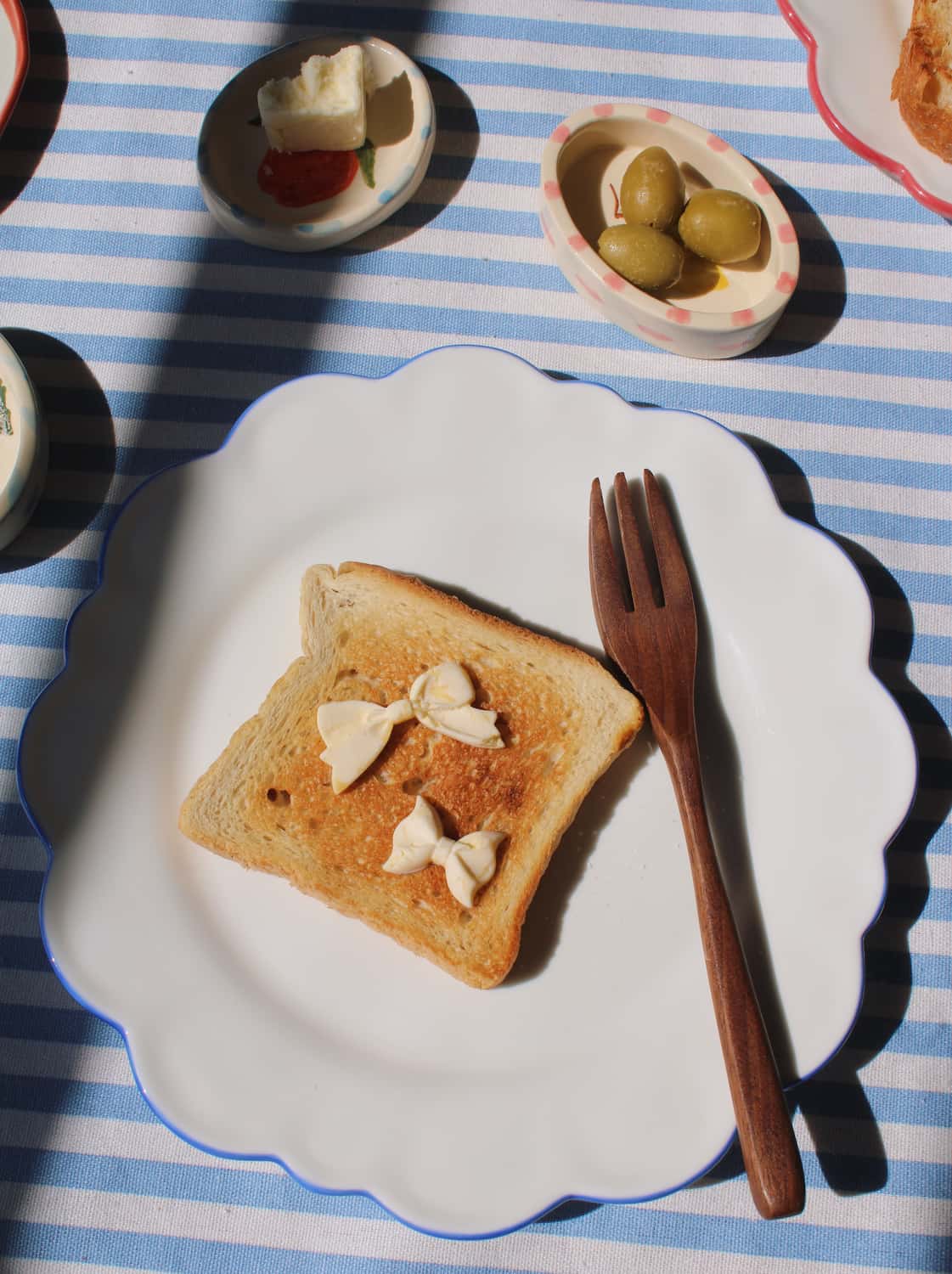 Toast with butter on a blue-rimmed white plate, Limonetta trinket dish with lemon design, set against a blue and white striped tablecloth. 