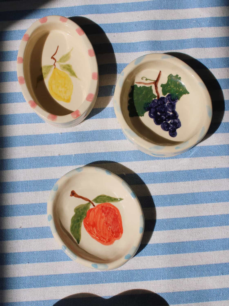 Three decorative ceramic plates with fruit illustrations on a blue and white striped background.