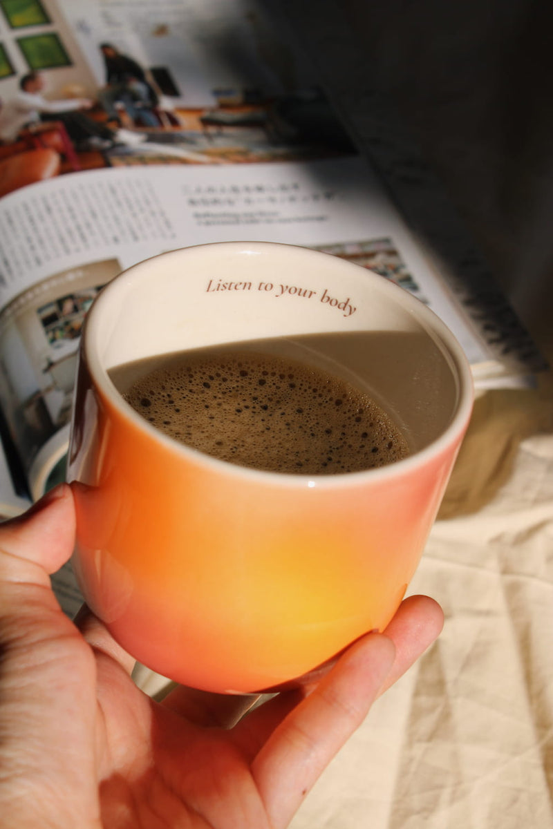 Gradient ceramic mugs in warm orange yellow and pink tones with "Listen to your body" printed inside the rim, handmade in small batches — Listen to Your Body limited edition ceramic mug bladder cancer awareness collection