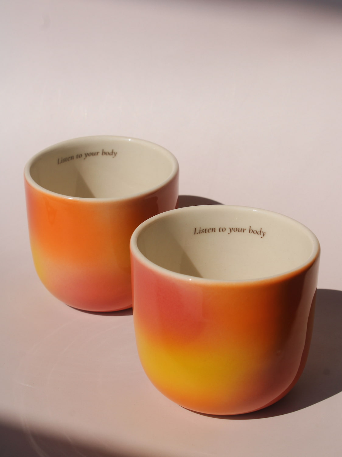 Gradient ceramic mugs in warm orange yellow and pink tones with "Listen to your body" printed inside the rim, handmade in small batches — Listen to Your Body limited edition ceramic mug bladder cancer awareness collection