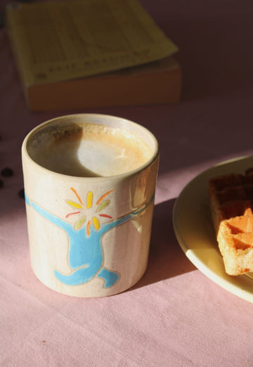 Cup of coffee with a colorful lyra ceramic mug on a pink surface with a book and plate in the background.