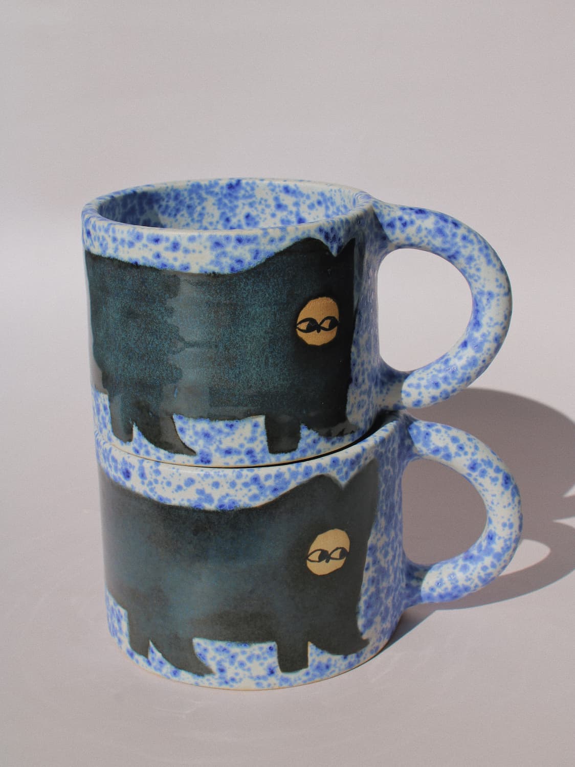     Midnight Cat Ceramic Mugs by Marta Shurpakova – two handmade blue ceramic mugs with playful black cat designs
