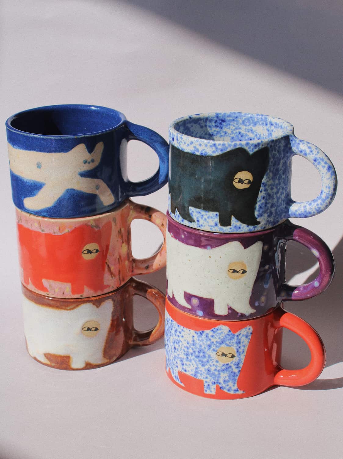 Ceramic Cat Mugs by Marta Shurpakova – six stacked handmade ceramic mugs with hand-painted cat designs 