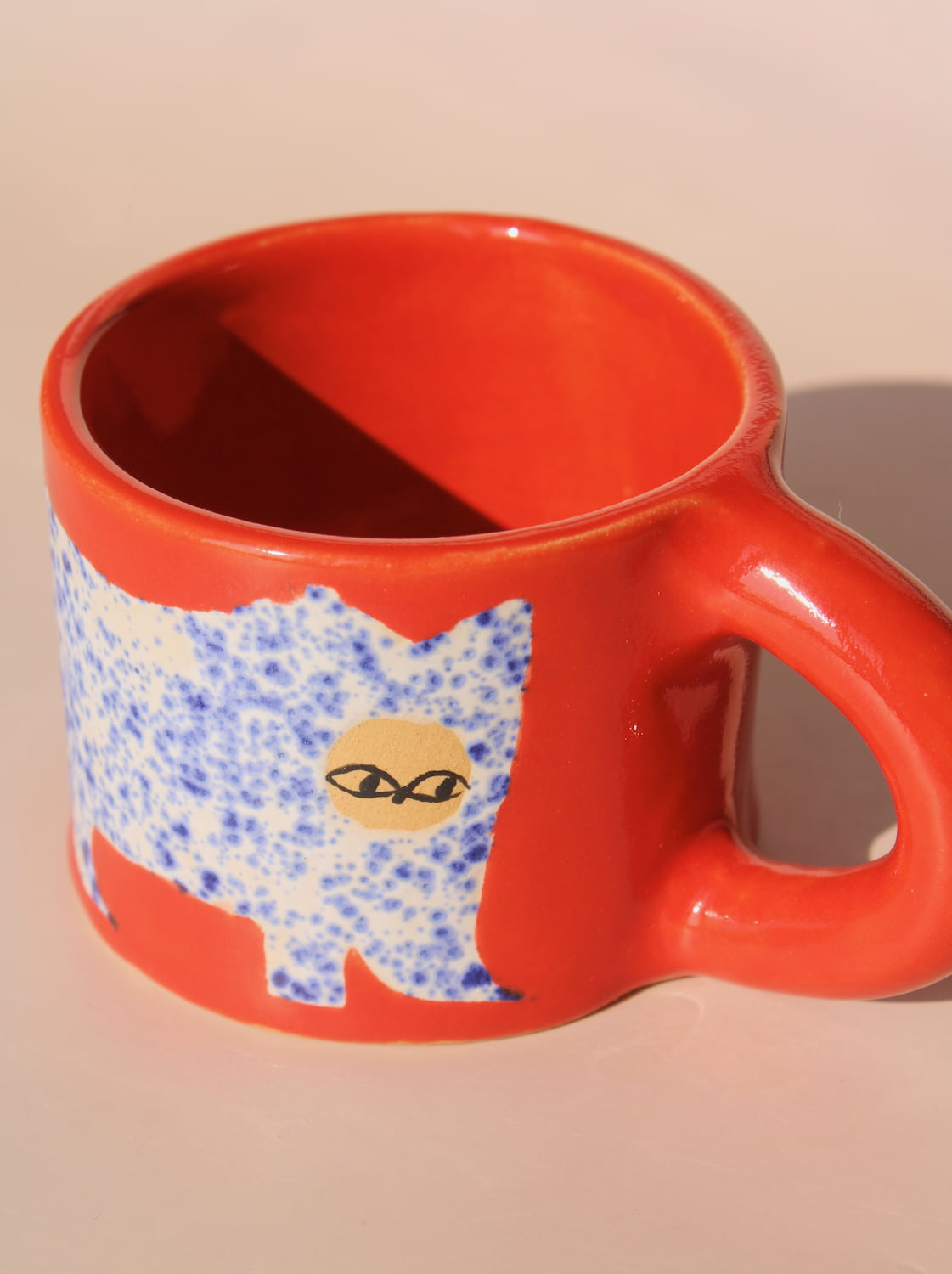 Red mug with a blue and white cat design on a beige background