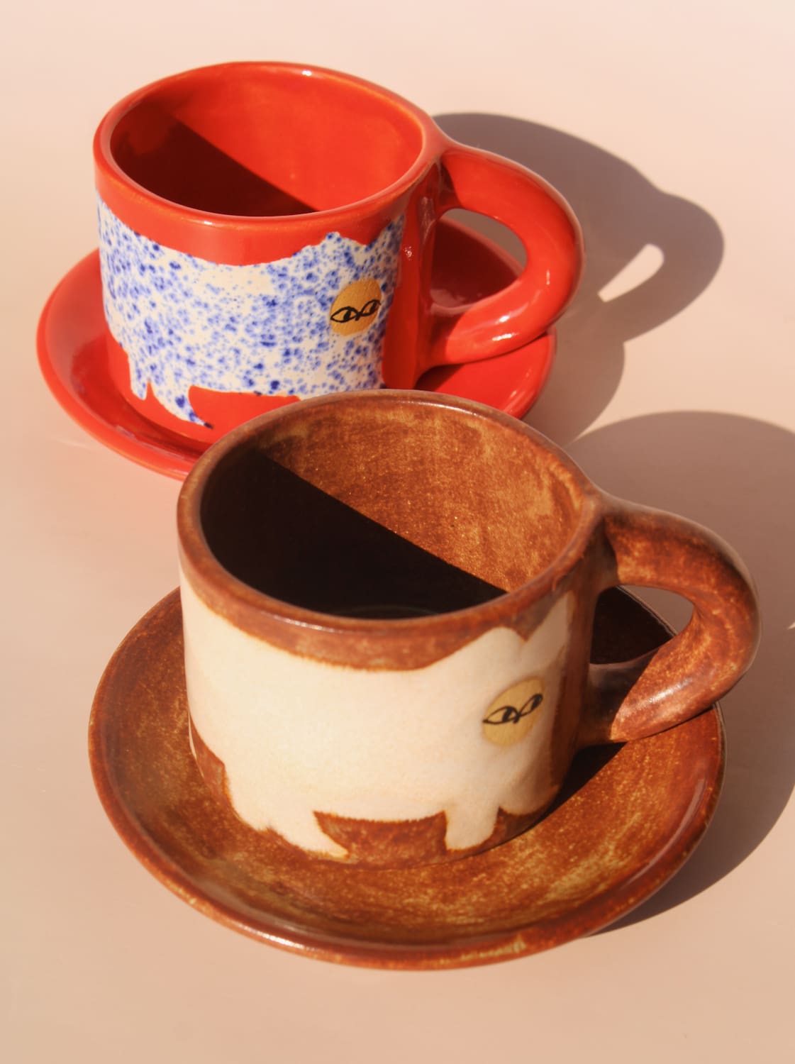 Two ceramic mugs with saucers on a beige background