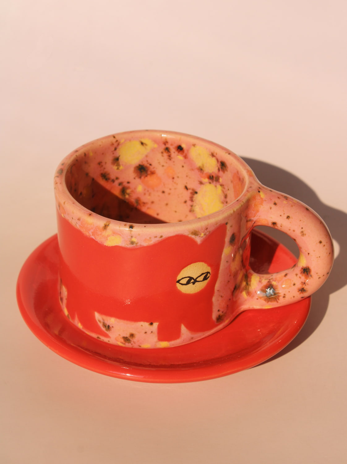 Speckled red cup and saucer with a handle on a beige background