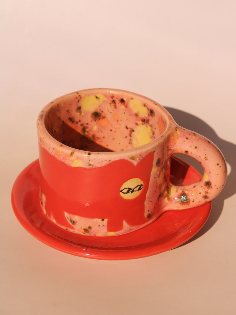 Speckled red cup and saucer with a handle on a beige background