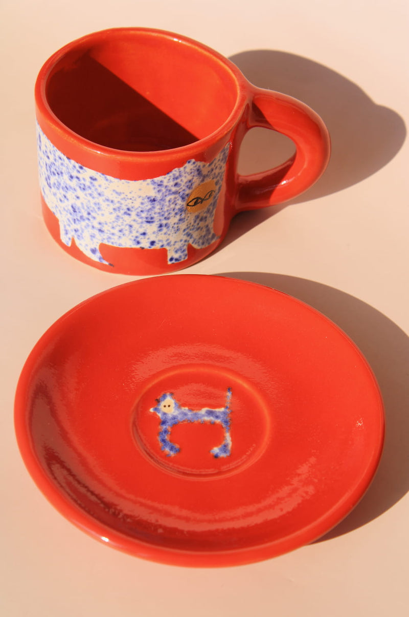 Red ceramic mug and saucer with a dog design on a beige background