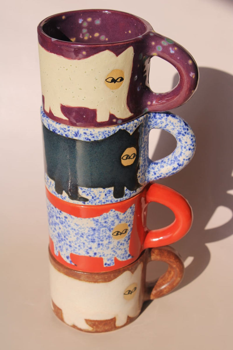 Stack of four ceramic mugs with cat illustrations on a beige background