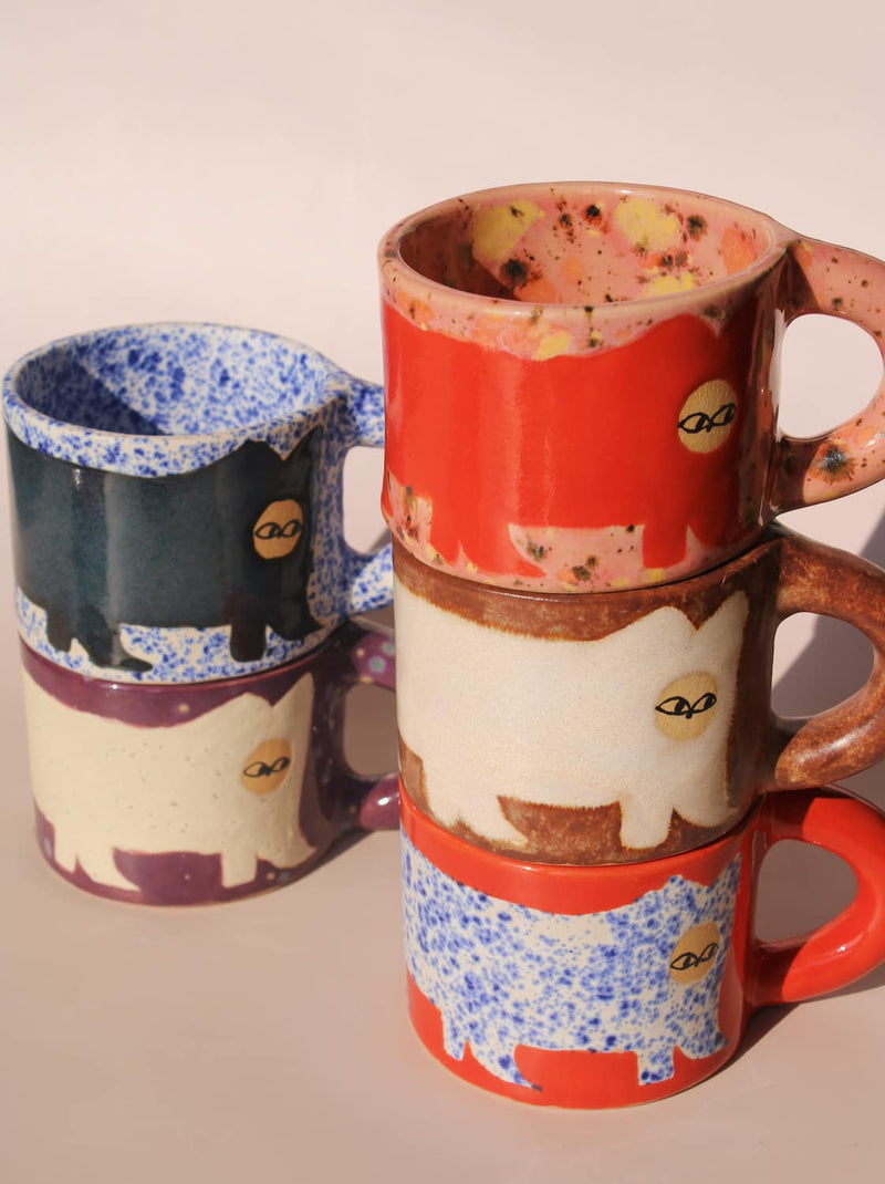 Two ceramic mugs with cat designs stacked on a beige background