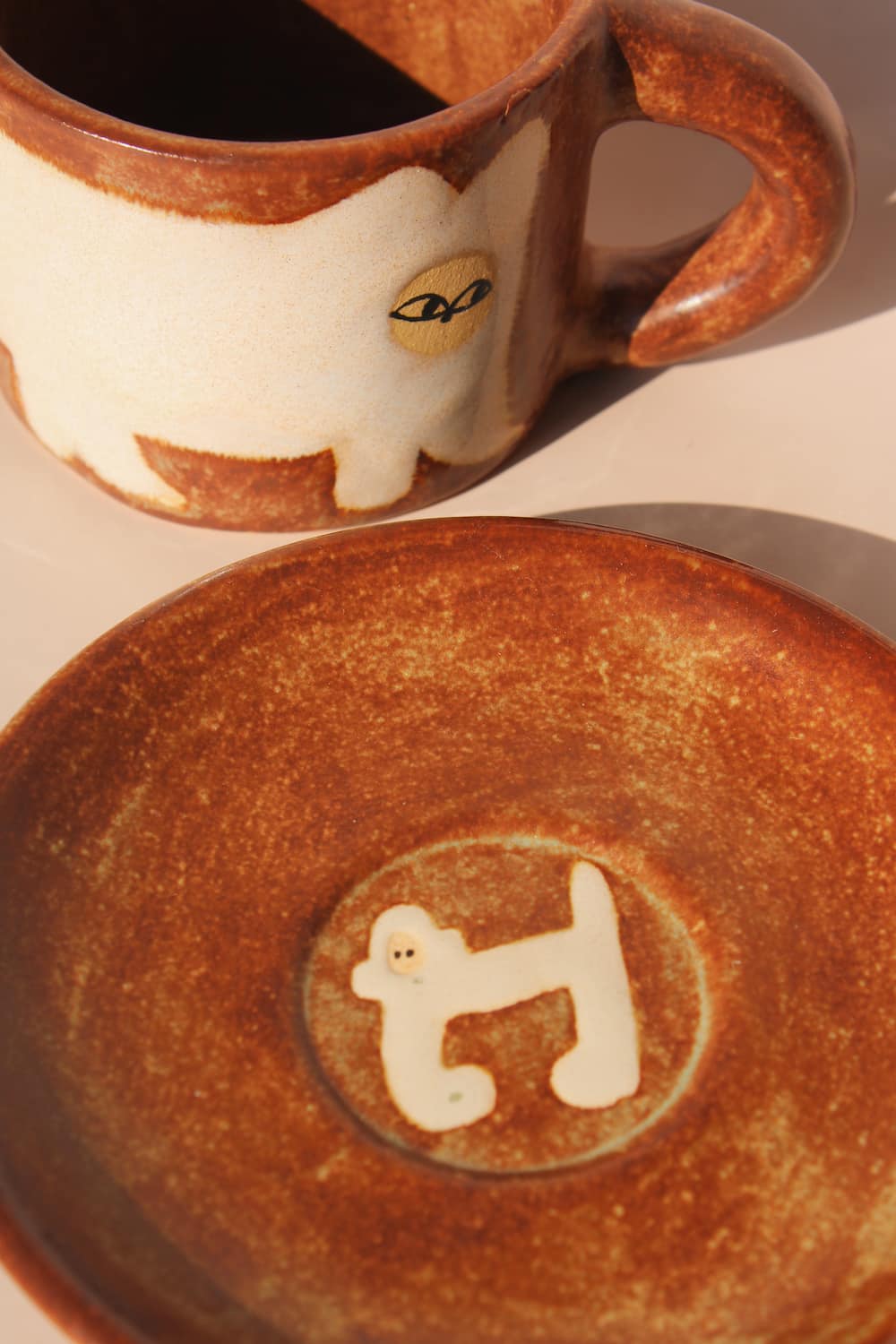 Ceramic mug with a cat design and matching plate with dog design on a beige background