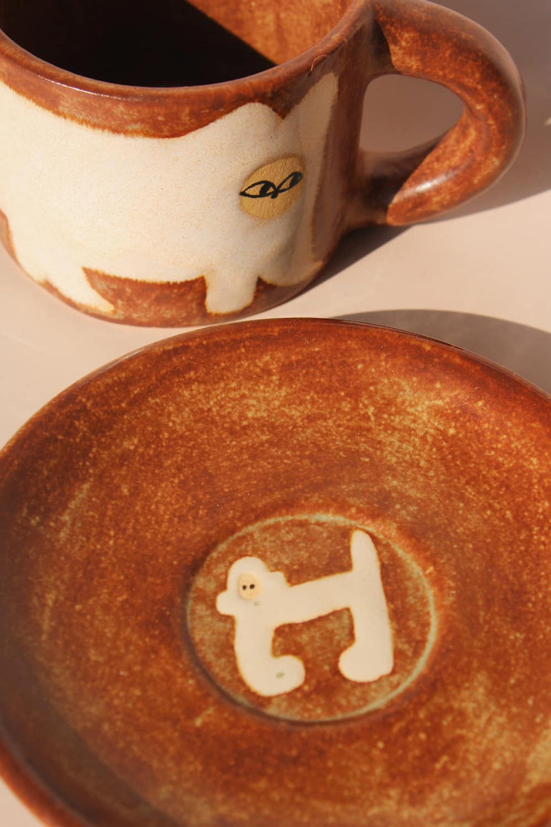 Ceramic mug with a cat design and matching plate with dog design on a beige background