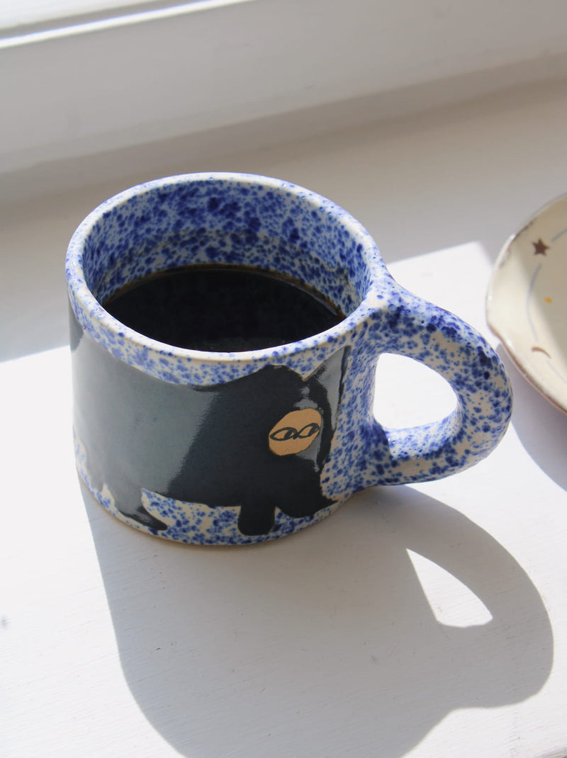 Blue speckled mug with a bear design on a white surface