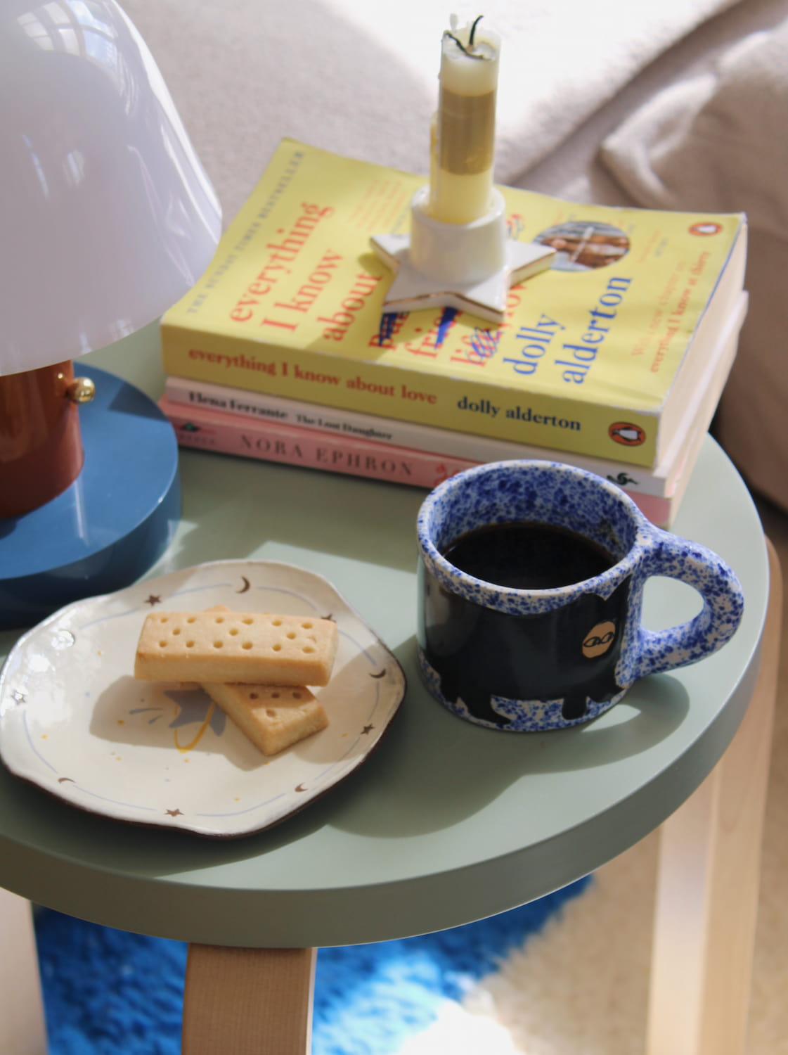 Small round table with a mug, cookies, and books on a light-colored surface.