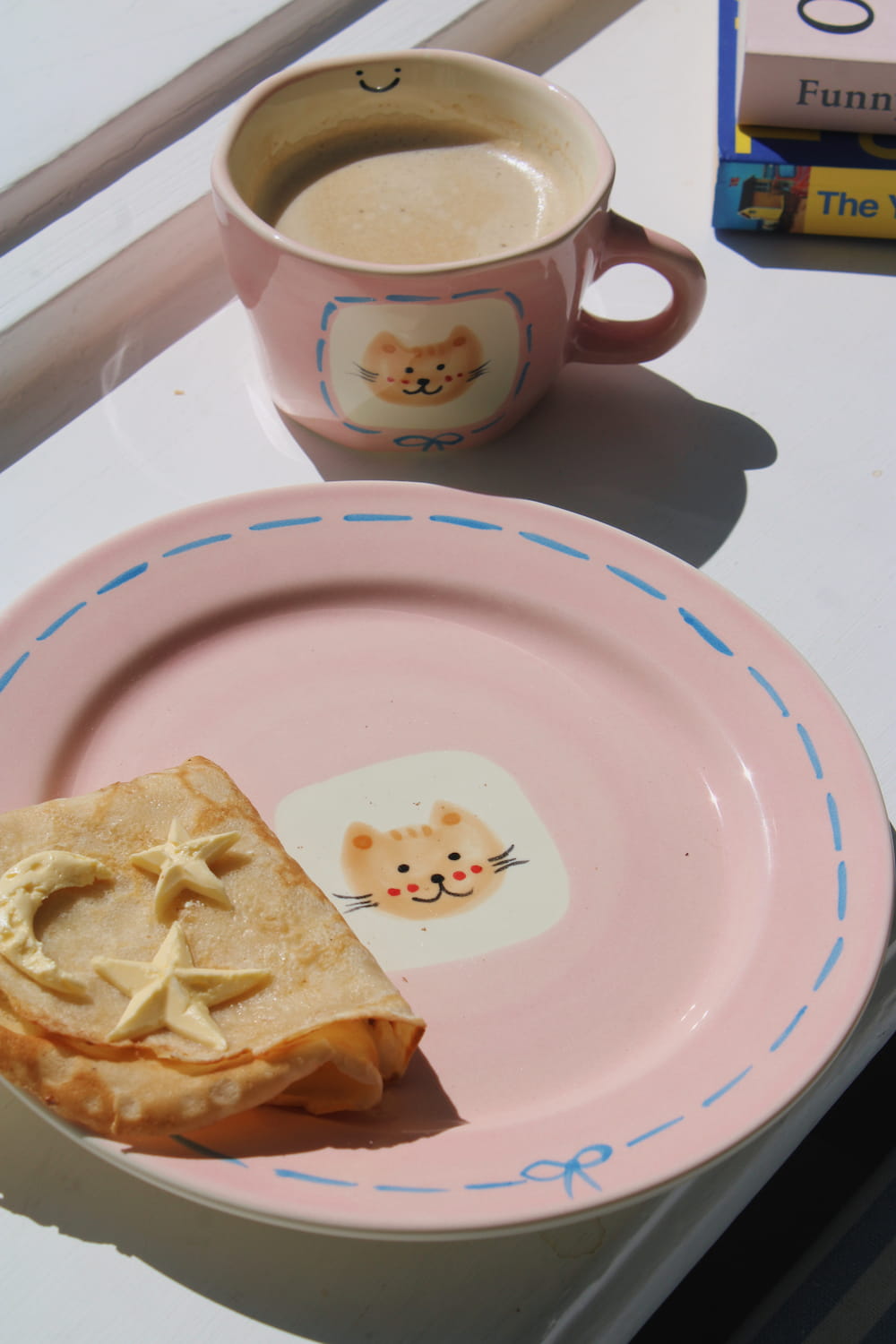 Mimi Ceramic Mug filled with coffee beside the Mimi Ceramic Plate styled with a buttered crepe on a blue striped surface, with ivy in the background.