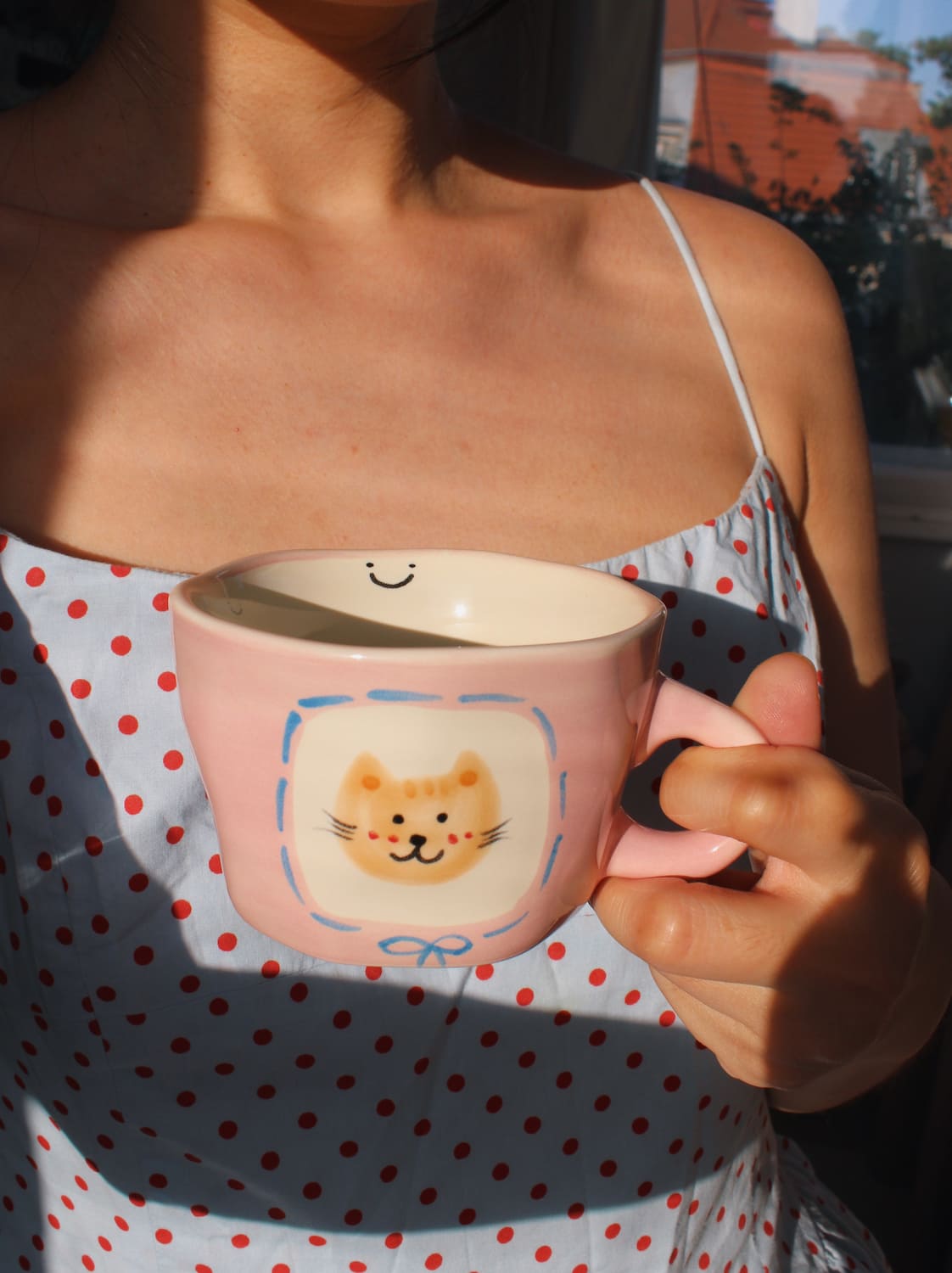 Person holding a pink mug with a cat design outdoors