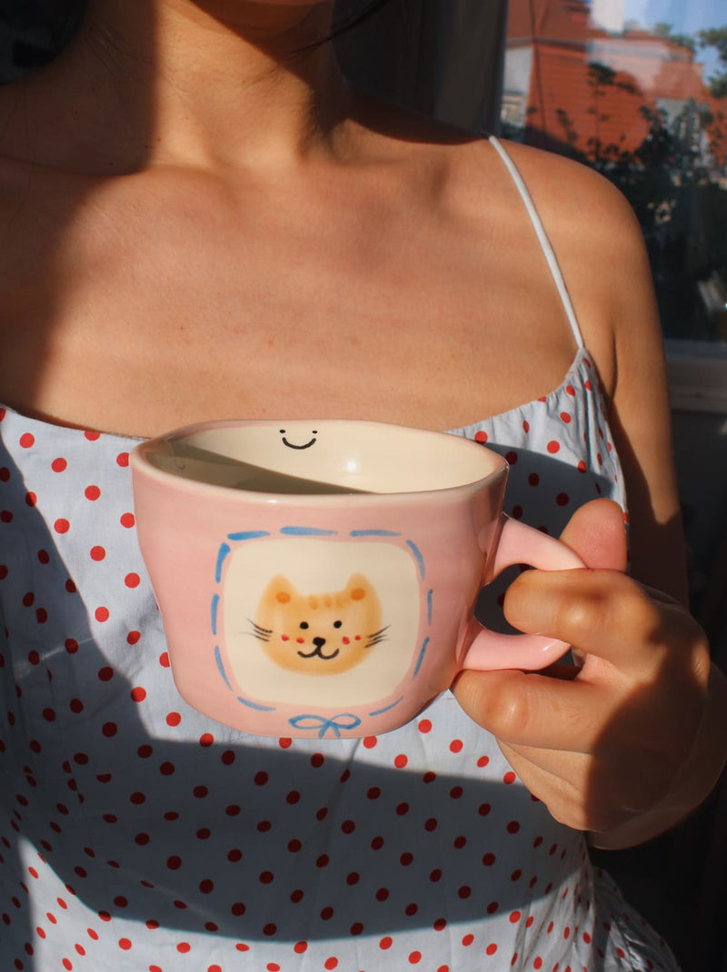 Person holding a pink mug with a cat design outdoors