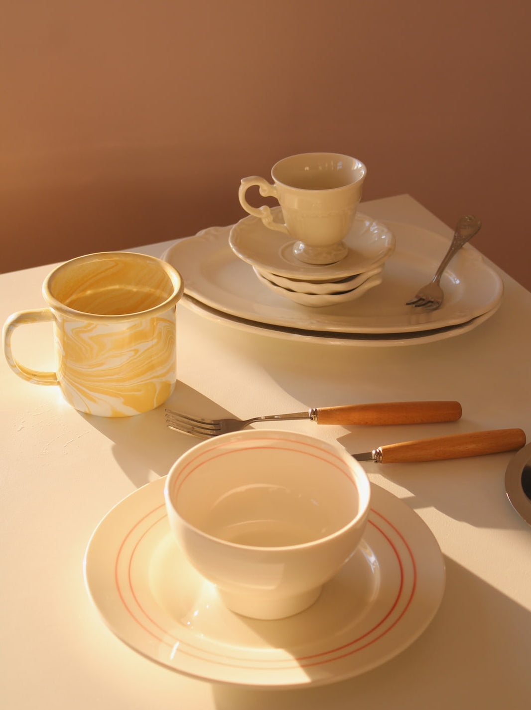 Handmade ceramic cups and plates styled on a sunlit table, featuring cream stoneware, vintage-inspired tableware, and warm neutral tones